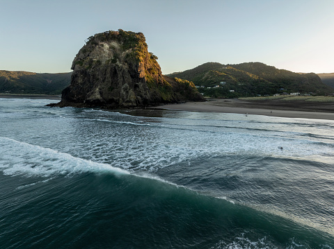 Piha/s iconic Lion Rock shot from the air on a crisp clear morning with fun surf rolling in.