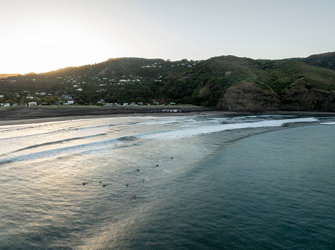 Surfers enjoying the waves at sunrise at Piha Beach, Auckland, New Zealand.