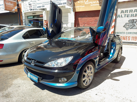 Remedios de Escalada, Argentina - Oct 8, 2023: Modern blue 2010s Peugeot 206 coupe cabriolet vertical opening doors 1999 - 2017 in the street on a sunny day. Classic car show