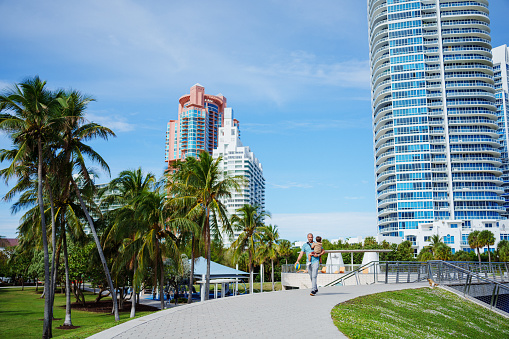 A loving and affectionate Caucasian father carries his Puerto Rican toddler son while walking on a city boardwalk with tall buildings behind them in Florida.