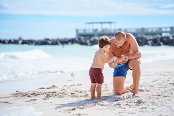 istock Toddler boy and father look at a shell on the beach 2038909256