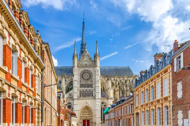 Amiens cityscape of old historical city centre with narrow pedestrian street, typical buildings and Amiens Cathedral Basilica of Our Lady Notre-Dame, blue sky, Hauts-de-France Region, Northern France