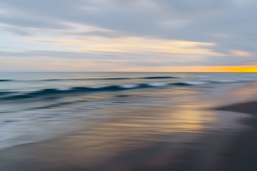 The last rays of the sunset cast a vibrant glow over the blurred motion of ocean waves