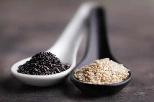 Sesame seeds in black and white spoons