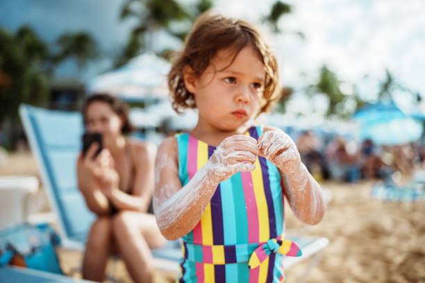 istock Cute girl rubs sunscreen on her arms while at the beach 2038951383