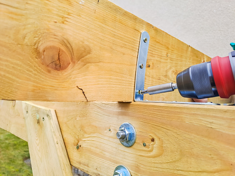 Worker using drill working on construction of wood frame house,Gazebo. Hands of caucasian worker drilling a wooden detail with a cordless electric drill-driver on a wooden workbench.High quality photo