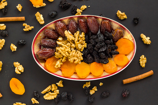 Above view of Traditional Dried Date Fruits designed in the stylish plate with apricot,walnut and grapes on the black surface.Ramadan Concept.