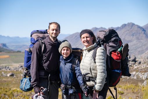 A portrait of a family of three with backpacks and hiking gear, they are on a hike in the mountains near Cape Town. Family exploring the outdoors.