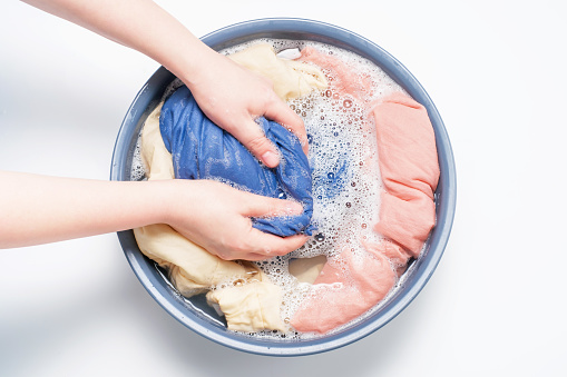Female hands washing clothes in basin on a white background, top view.