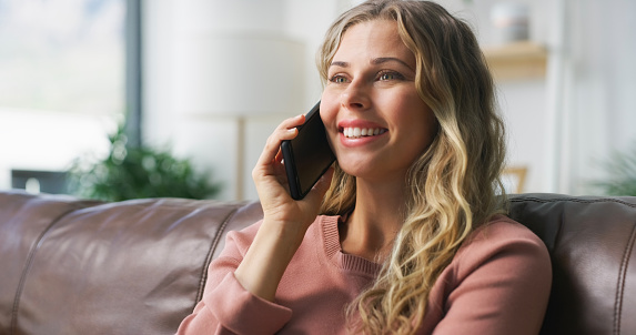 Phone call, happy and young woman on a sofa in the living room relaxing in her apartment. Smile, communication and female person from Canada on a mobile conversation with cellphone in lounge at home.