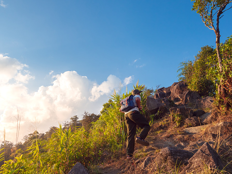 Asian man with backpack traveling solo on a tropical mountain peak in the sunset
