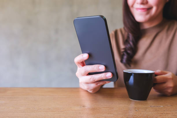 istock Closeup image of a young woman holding and using mobile phone while drinking coffee 2039399258