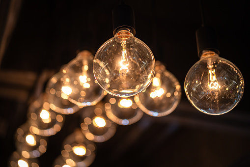 Classic sphere lighting bulbs are glowing in orange warming shade, there are hanging from ceiling in dark environment. Interior cozy style decoration. Close-up and selective focus.