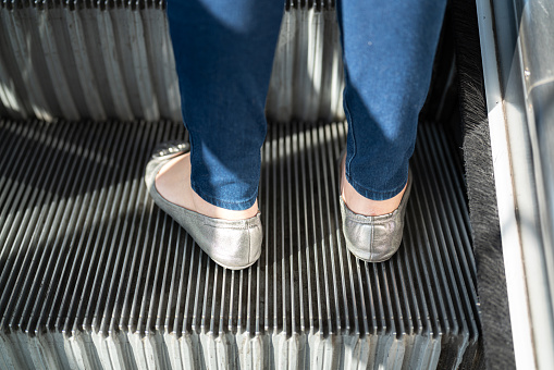 Close-up at a female heel, wearing court shoes during standing on the escalator floor.