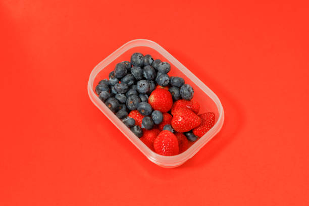 Top view, Mix of blueberries and strawberries in a recycled plastic box on the red background, Vitamin-rich fruits are packed in boxes.