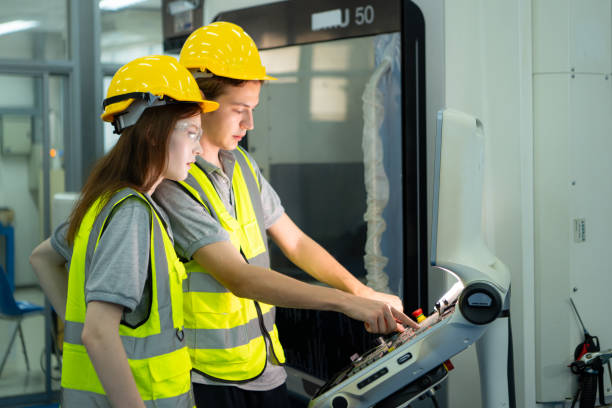 both of  young factory worker wearing a hard hat looking at a computer screen used to control production. - computer control room hardhat computer monitor 뉴스 사진 이미지