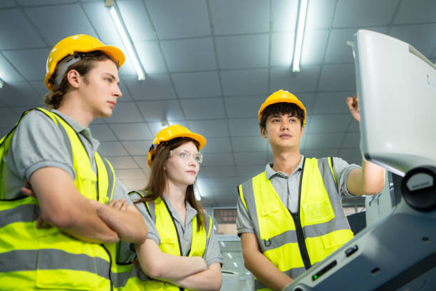 both of  young factory worker wearing a hard hat looking at a computer screen used to control production. - computer control room hardhat computer monitor 뉴스 사진 이미지