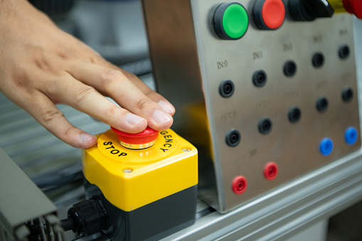 Close-up of hand pressing the stop button on the control panel of an industrial machine.