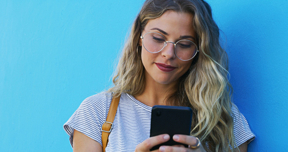 Phone, search and woman in a city for travel, texting or social media browsing on blue background space. Smartphone, app and female traveler online for taxi, service or chauffeur request on commute