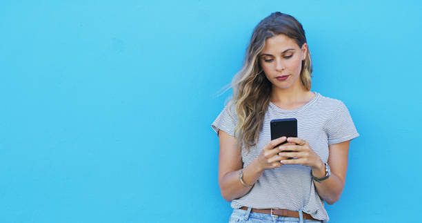istock Woman, phone and reading with space by wall, chat and texting for communication on mobile network. Girl, smartphone and typing for contact, mock up and thinking with social media by blue background 2039509669