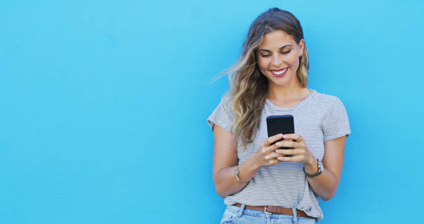 istock Woman, phone and chat with space by wall, smile and texting for communication on mobile network. Girl, smartphone and happy for contact, mock up and thinking with social network by blue background 2039509676