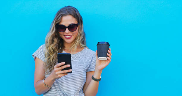 istock Girl, phone and coffee with thinking by wall, sunglasses and texting for communication on mobile network. Woman, smartphone and happy with latte, mockup and contact on social media by blue background 2039509679