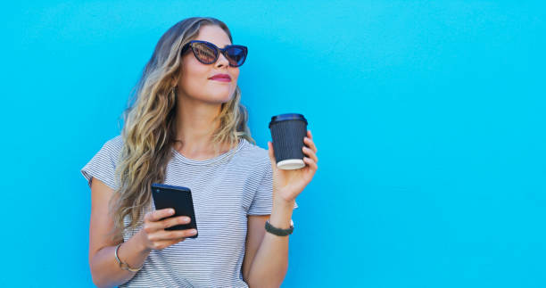 istock Woman, phone and coffee with thinking by wall, sunglasses and texting for communication on mobile network. Girl, smartphone and happy for matcha, mockup and contact on social media by blue background 2039509680