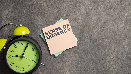 Alarm clock with 'sense of urgency' text on the stack of notepaper with a black background. Urgency concept