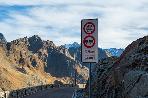 Asphalt road and road sign high in mountains with rocky peaks.