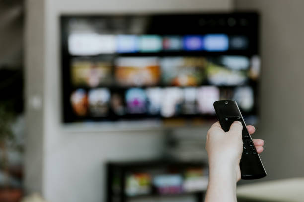 istock Hand holding remote control pointing to TV. Person watching smart television 2039584739
