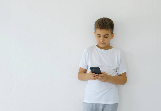 istock Cute little boy playing with a smartphone over white wall background 2039600486