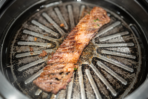 A piece of cut premium meat which is grilling on metal plate of the heating oven. BBQ food meal cooking photo. Close-up and selective focus.