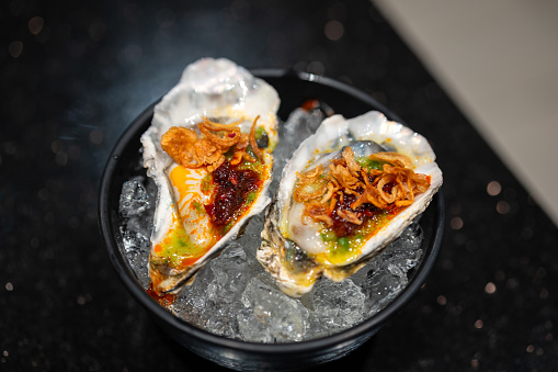 Fresh raw oysters that topping with spicy seafood sauce and other ingredient, served on iced. Thai food menu. close-up and selective focus.