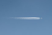 A distant airplane flying horizontally , aeroplane leaving a vapour trail from its four jet engines far up in a deep blue sky