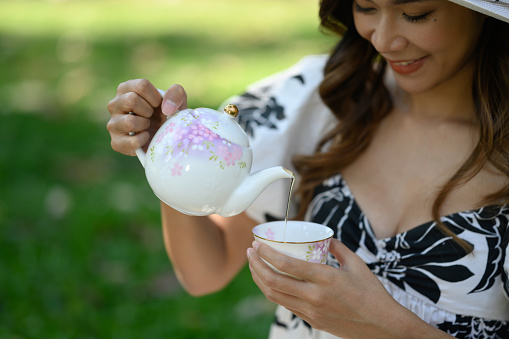 Young beautiful woman pouring hot tea into a cup while sitting in the garden.