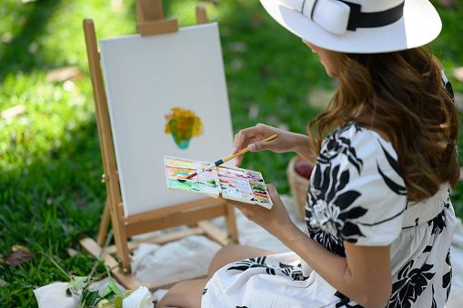 Young woman painting a picture in the park. Mindfulness, art therapy and creative hobbies concept.