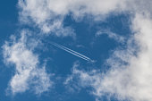 A distant airplane, aeroplane leaving a vapour trail from its four jet engines far up in a deep blue sky encased by the surrounding clouds