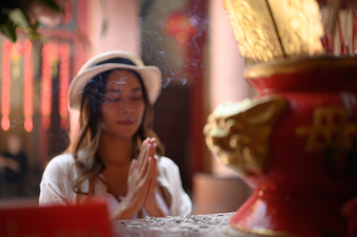 Female tourist praying at a shrine at Chinese temple for blessing, grace and gratitude.