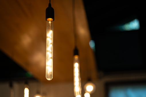 Ceiling lighting bulbs are glowing in orange warming shade in dark environment. Interior cozy style decoration. Close-up and selective focus.