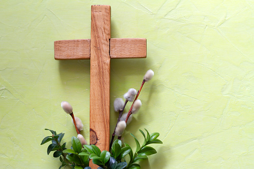 Wooden cross with boxwood twigs and catkins on green background. Palm Sunday concept idea