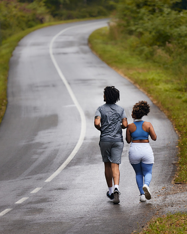Rear view of African American couple of athletes jogging in autumn day on empty road.