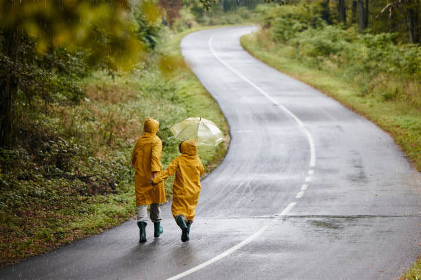 vista posteriore della coppia spensierata che cammina sulla strada durante il giorno di pioggia. - candid women african descent umbrella foto e immagini stock