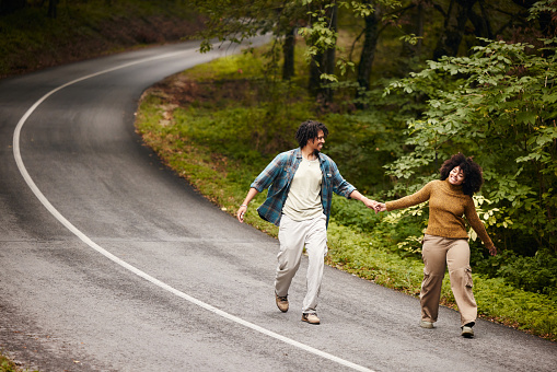 Happy African American couple having fun while running on empty road in autumn day. Copy space.