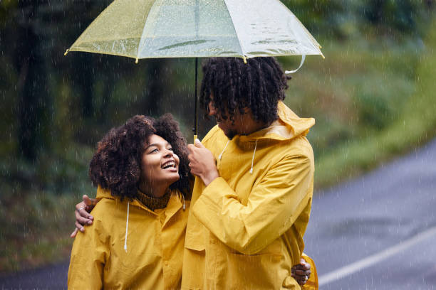 happy couple walking in the park in rainy day carrying transparent umbrella