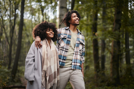 Happy African American couple enjoying while walking embraced during autumn day in nature.