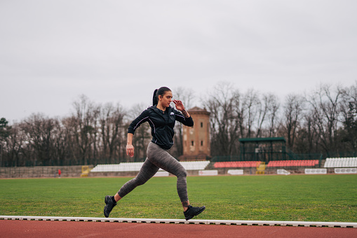 A young athlete is training on the track. She runs. Picture from the side.