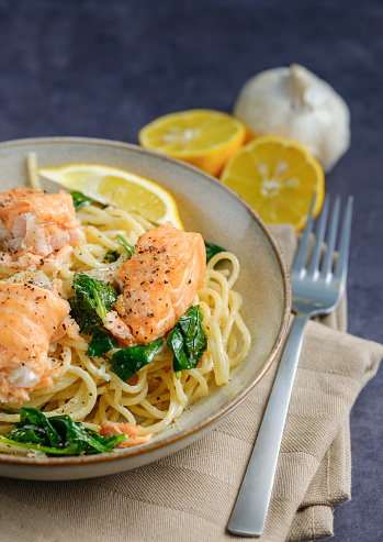 Italian cuisine: spaghetti with salmon, cream and spinach close-up on plate on table. vertical close up