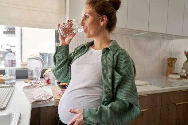 istock Pregnant woman drinking water while standing in the kitchen 2039723903