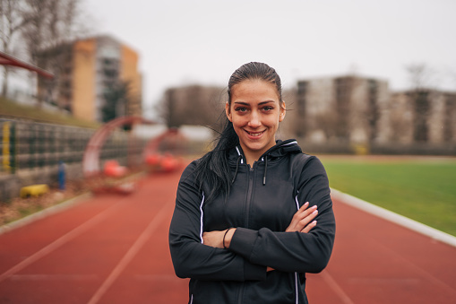 Portrait of a young woman with crossed arms, on a running track.