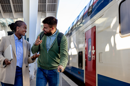 The image portrays a Caucasian man and an African American woman after their journey, moving side by side as they exit the train station